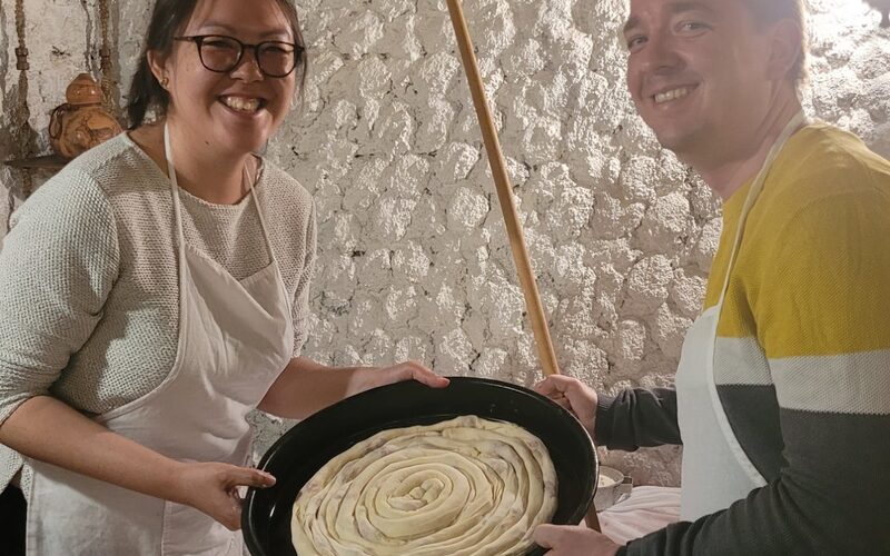 Guests proudly holding a freshly rolled burek spiral in a traditional pan